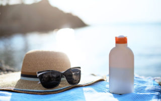 Sunčana plaža na kojoj se nalaze ručnik, tamne naočale i krema za zaštitu od sunca, suncobran u pozadini