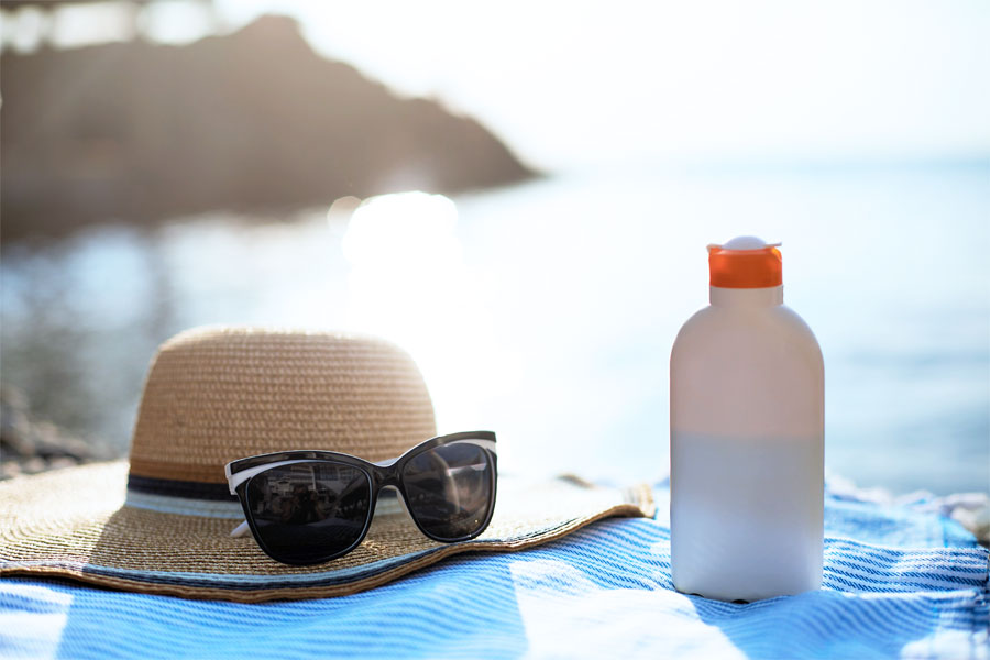 Sunčana plaža na kojoj se nalaze ručnik, tamne naočale i krema za zaštitu od sunca, suncobran u pozadini